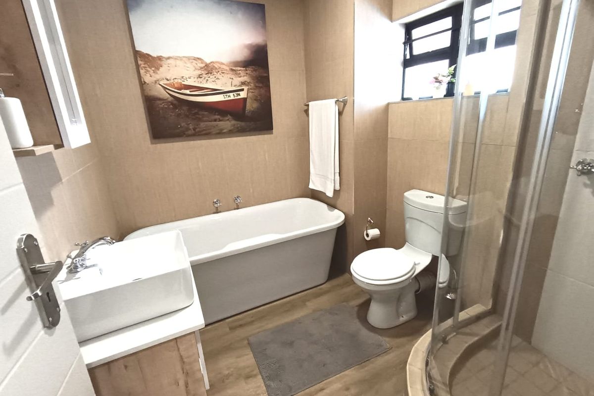 A well-appointed bathroom featuring a freestanding bathtub, a separate glass-enclosed shower, a modern vessel sink vanity, and neutral wall tiling.