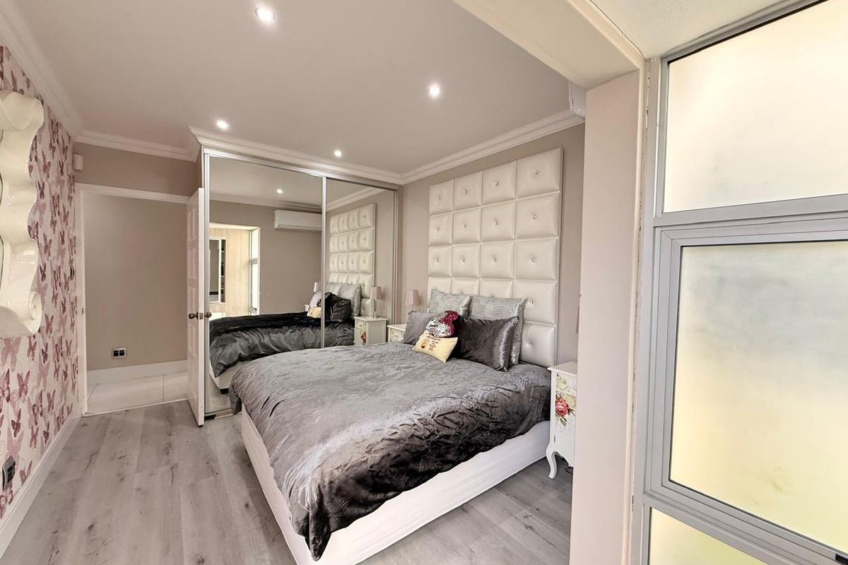 A well-maintained bedroom featuring built-in mirrored wardrobes, recessed ceiling lighting, and modern laminate flooring.