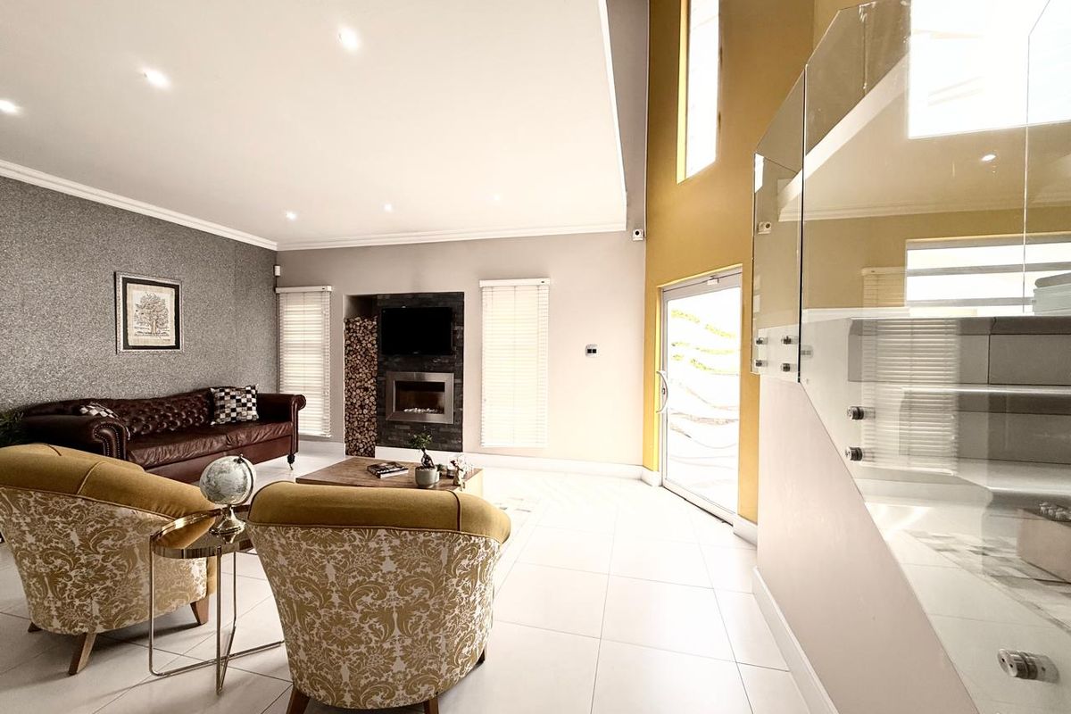 Spacious living area featuring a modern built-in fireplace, tiled flooring, high ceilings, and a glass balustrade staircase.