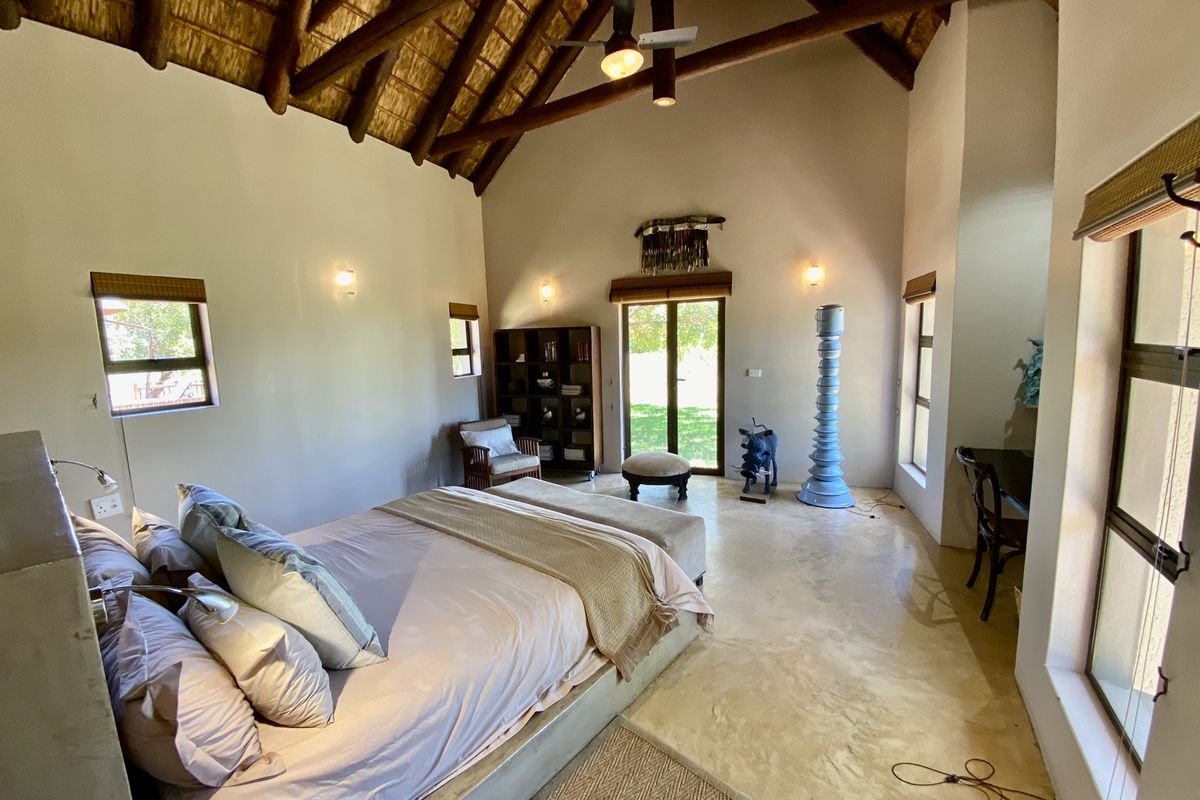 Spacious bedroom featuring a high vaulted thatched ceiling with exposed timber beams, polished concrete flooring, and direct access to the garden.