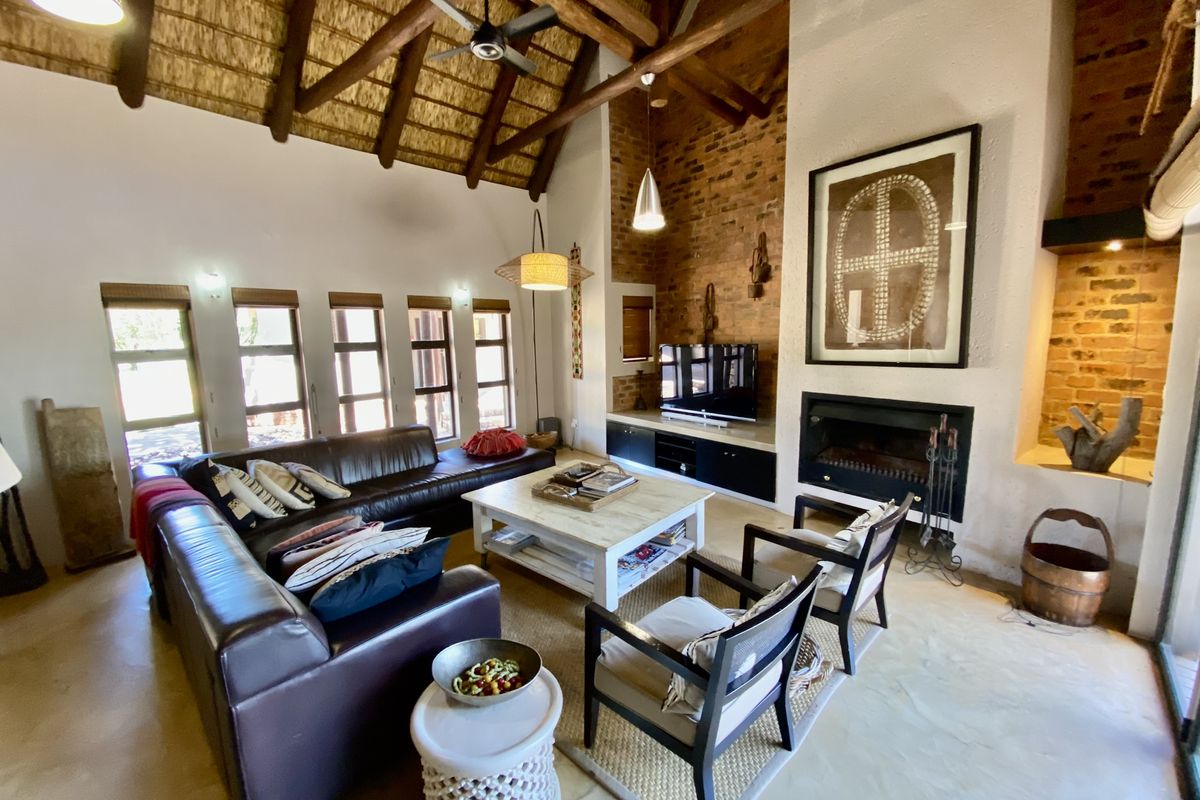 Spacious living room featuring a high vaulted thatched ceiling with exposed timber beams, a prominent brick fireplace, and polished concrete flooring.