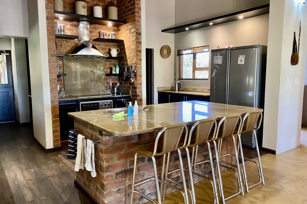 A rustic-style kitchen featuring an exposed brick island with a stone countertop, built-in oven, extractor fan, and open shelving.