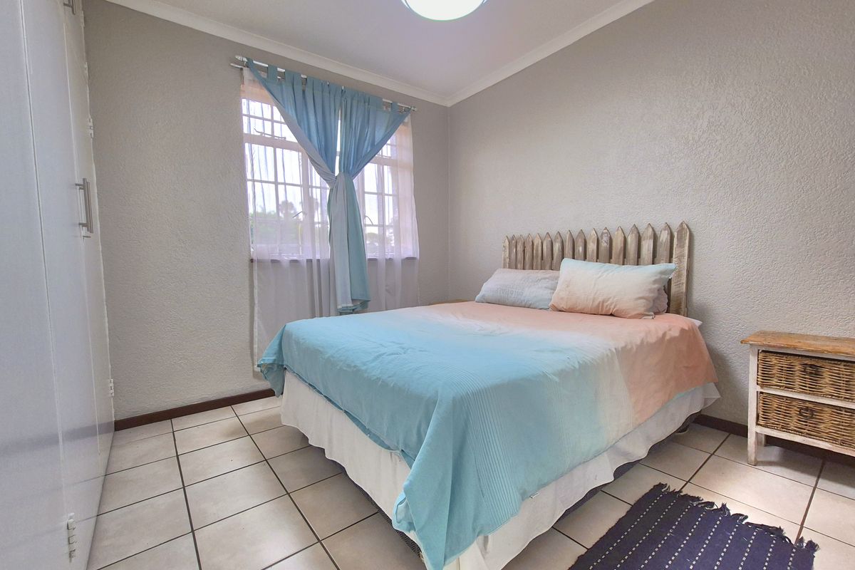 A functional bedroom featuring built-in cupboards, tiled flooring, and a window with security bars, providing a simple and practical living space.