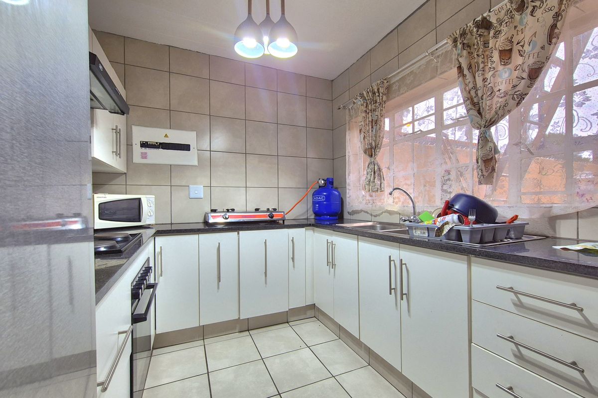 A functional kitchen featuring white cabinetry, dark countertops, tiled walls, and a double sink, providing a practical workspace for daily meal preparation.