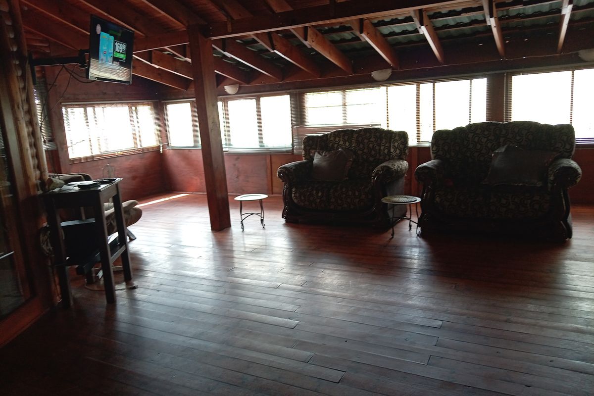 Spacious living area featuring exposed timber beam ceilings, warm wood flooring, and extensive window glazing providing ample natural light.