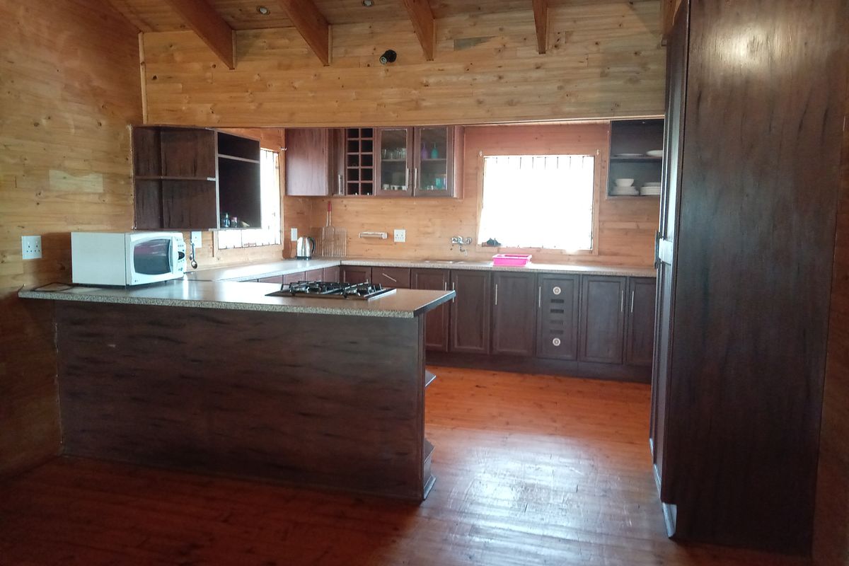 A rustic kitchen featuring dark wood cabinetry, a breakfast bar, integrated gas hob, and exposed timber ceiling beams within a timber-clad interior.