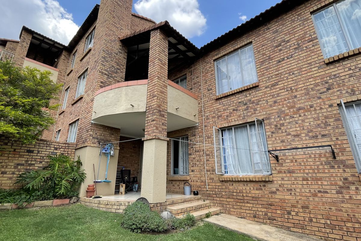 Rear view of a multi-story townhouse featuring face-brick facade, a covered patio area, and a private garden space.