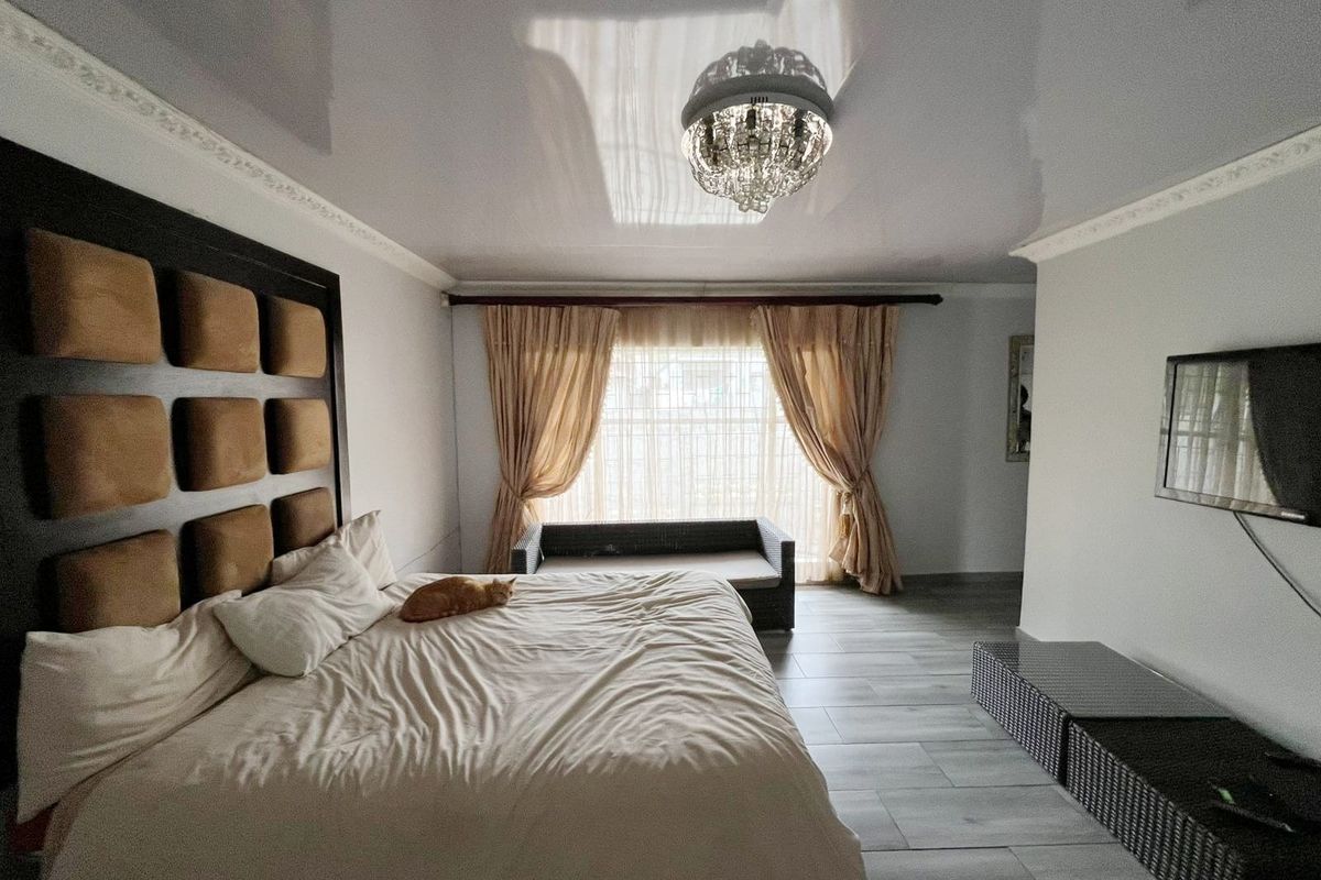 Spacious bedroom featuring a glossy ceiling finish, decorative crown molding, tiled flooring, and a large window with curtain treatments.