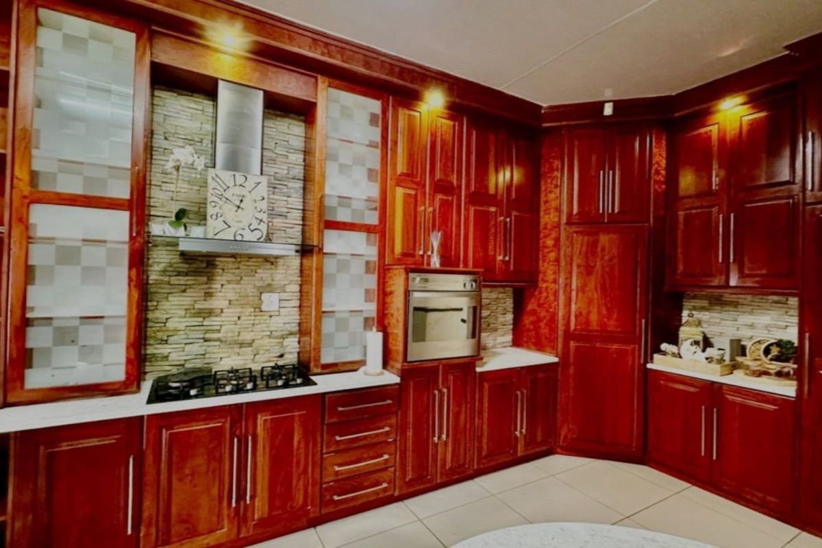 A traditional kitchen featuring rich wood cabinetry, stone-tiled backsplash, built-in oven, gas hob, and stainless steel extractor fan.