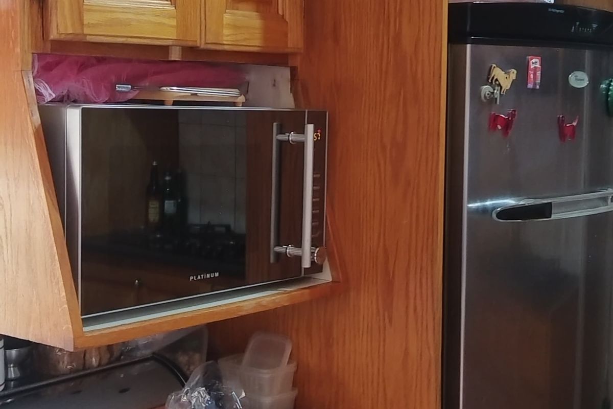 A kitchen area featuring traditional timber cabinetry, laminate countertops, and a built-in microwave shelf.