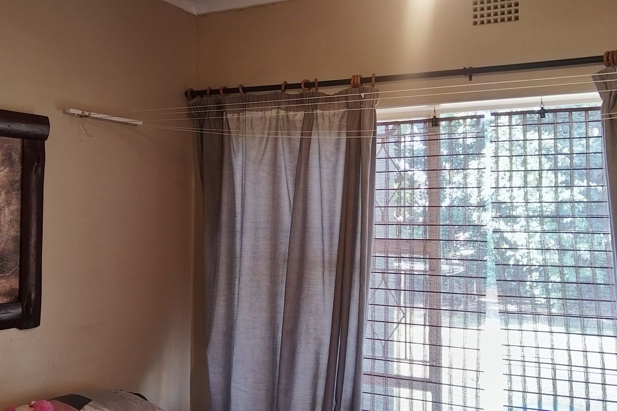 A bedroom interior featuring a window with security bars, curtain rod, and ceiling ventilation vent.