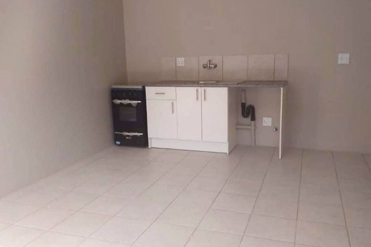 A simple, empty kitchen area featuring basic cabinetry, a sink, tiled splashback, and a freestanding stove on tiled flooring.
