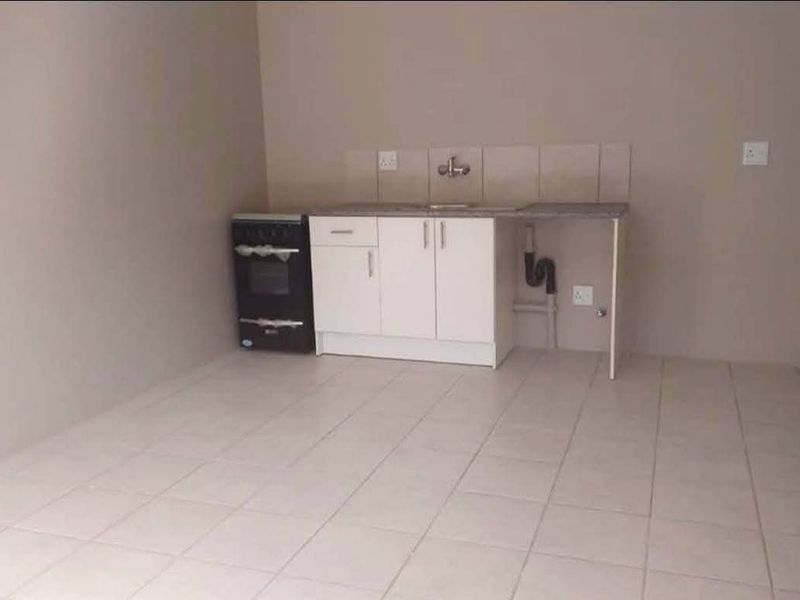 A simple, empty kitchen area featuring basic cabinetry, a sink, tiled splashback, and a freestanding stove on tiled flooring.