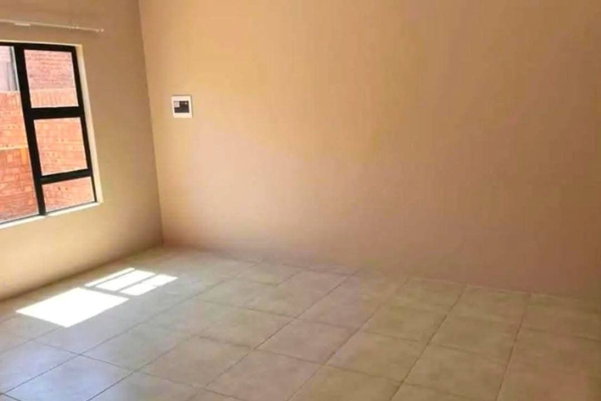 A vacant bedroom featuring neutral wall tones, tiled flooring, and a large window providing natural light.