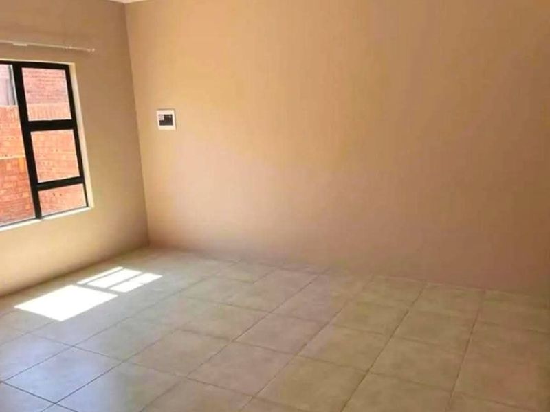 A vacant bedroom featuring neutral wall tones, tiled flooring, and a large window providing natural light.