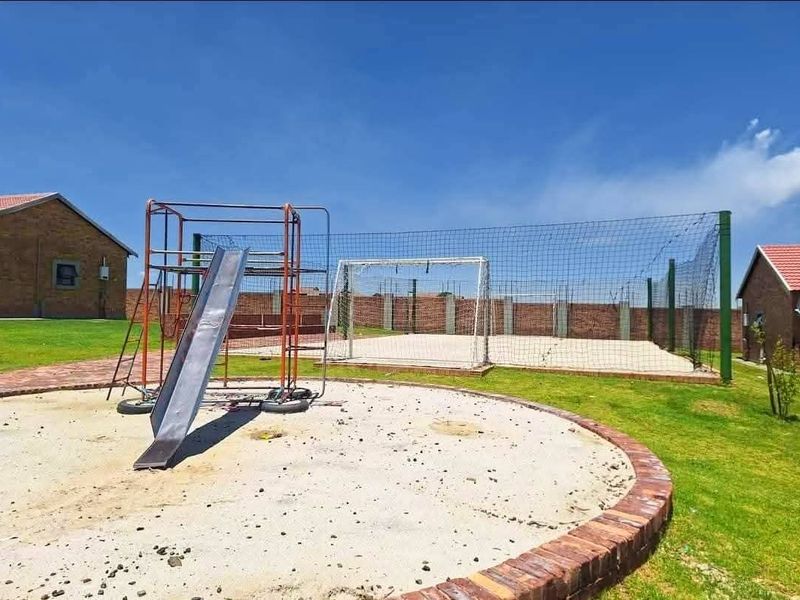Outdoor communal sports facility featuring a soccer goal with safety netting, a playground slide, and brick-edged landscaped areas within the townhouse complex.