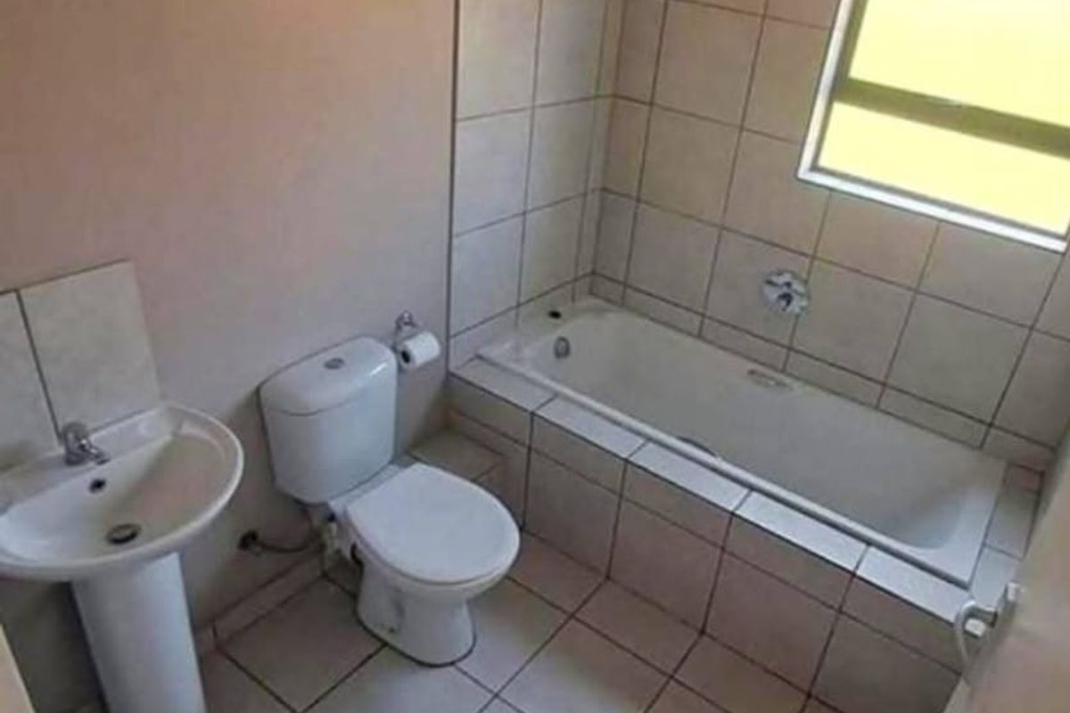 A functional bathroom featuring a pedestal basin, toilet, and a tiled bathtub area with a shower head.
