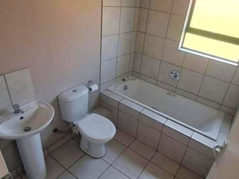A functional bathroom featuring a pedestal basin, toilet, and a tiled bathtub area with a shower head.