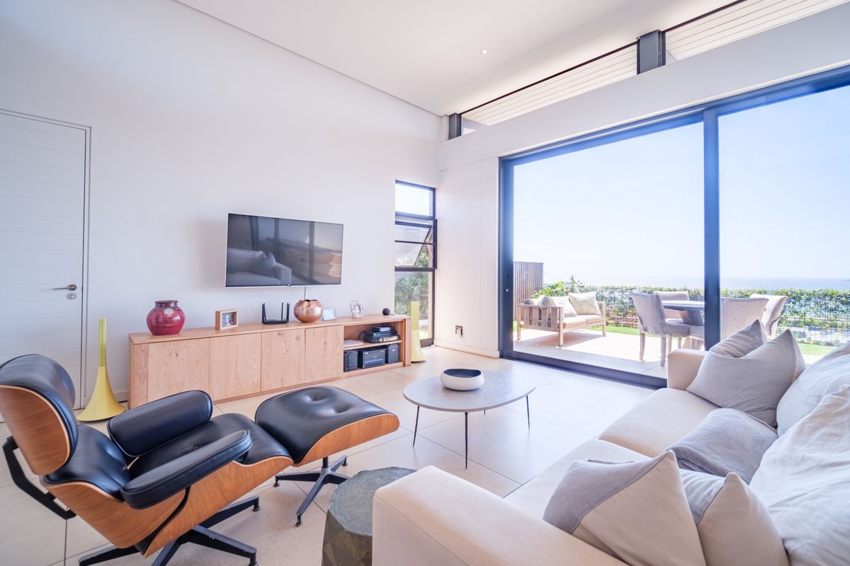 Modern living room featuring large sliding glass doors that open to an outdoor patio with scenic views, high ceilings, and tiled flooring.