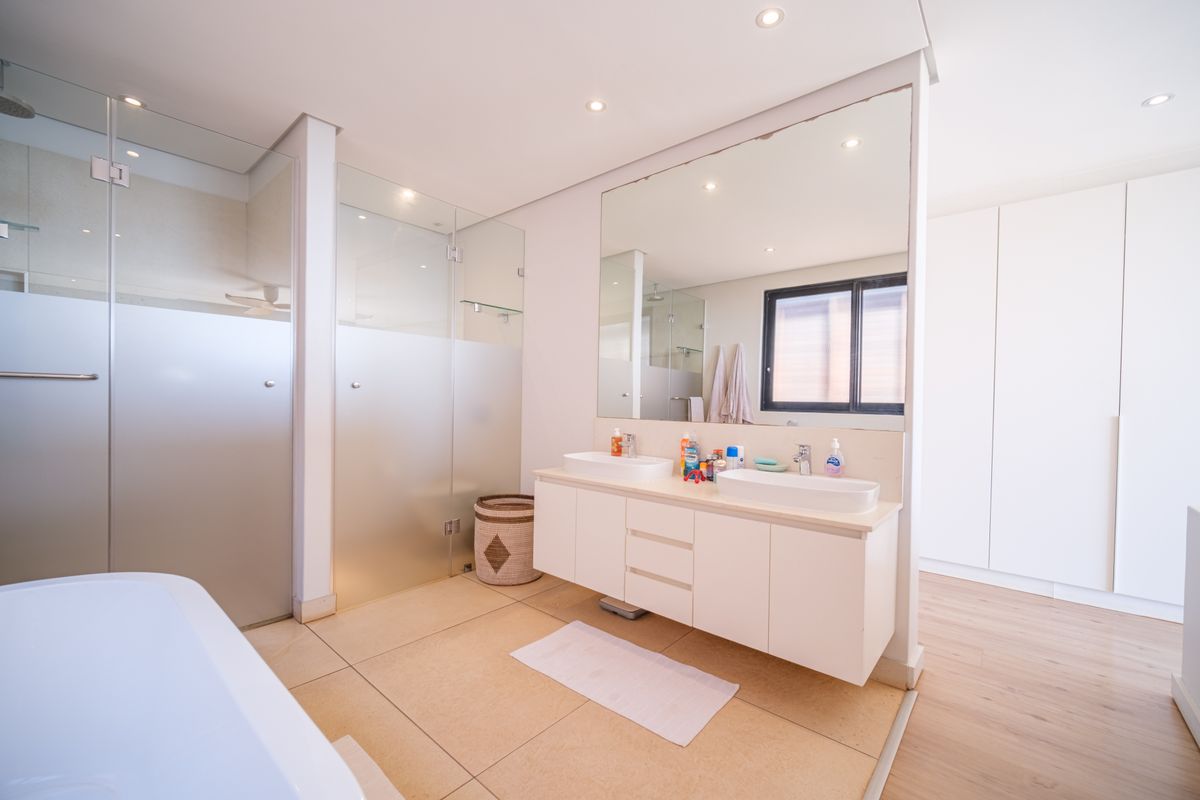 Modern bathroom featuring a double vanity with integrated sinks, a large wall-mounted mirror, and a separate glass-enclosed shower area.