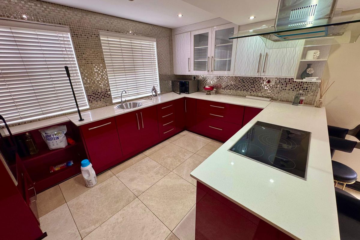 Modern kitchen featuring high-gloss red cabinetry, white stone countertops, a glass extractor fan, and a mosaic tile backsplash.