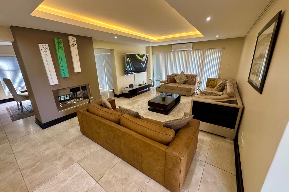 Spacious living room featuring a built-in fireplace, recessed tray ceiling with ambient lighting, tiled flooring, and wall-mounted air conditioning unit.