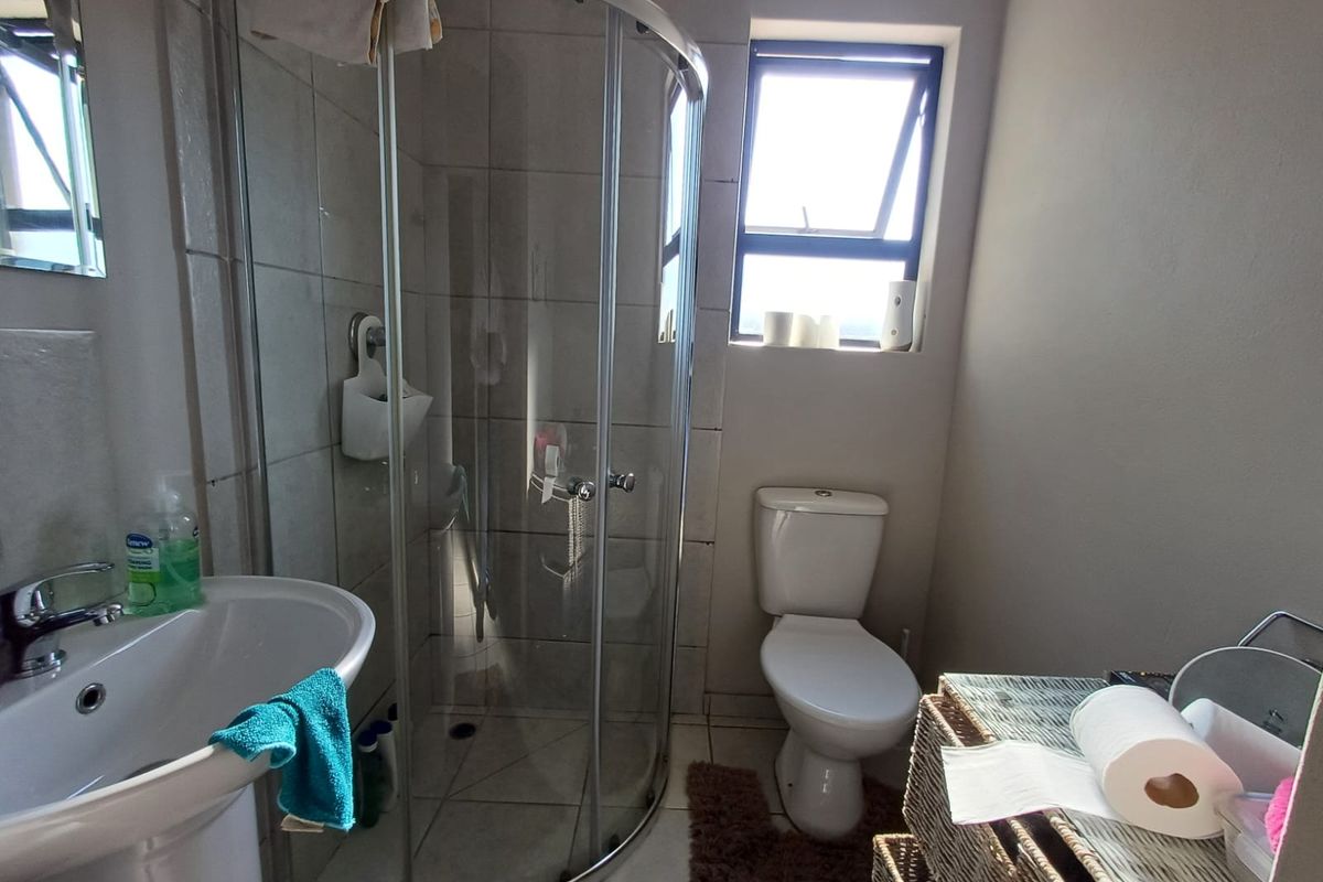 A functional bathroom featuring a corner glass shower enclosure, pedestal basin, and standard toilet with tiled flooring and natural light from a window.