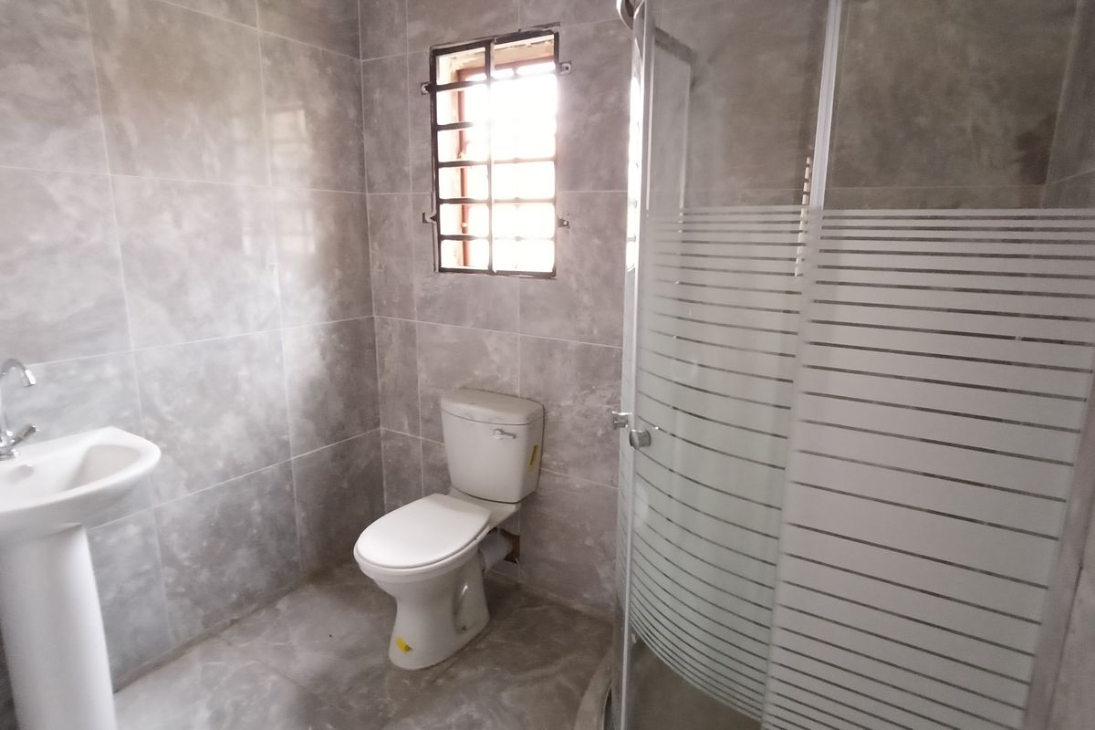 A modern bathroom featuring grey marble-effect wall and floor tiles, a pedestal basin, a white toilet, and a glass-enclosed shower unit.