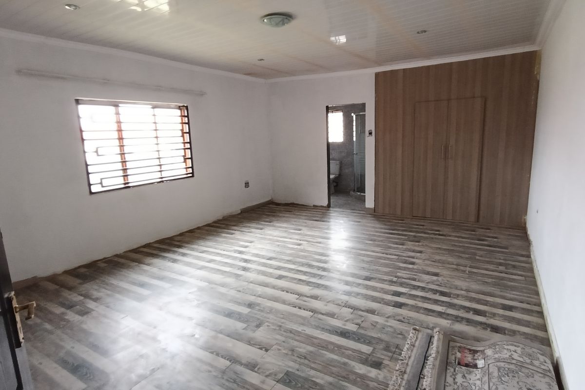A spacious, empty bedroom featuring wood-look laminate flooring, built-in wooden cupboards, and an en-suite bathroom entrance.