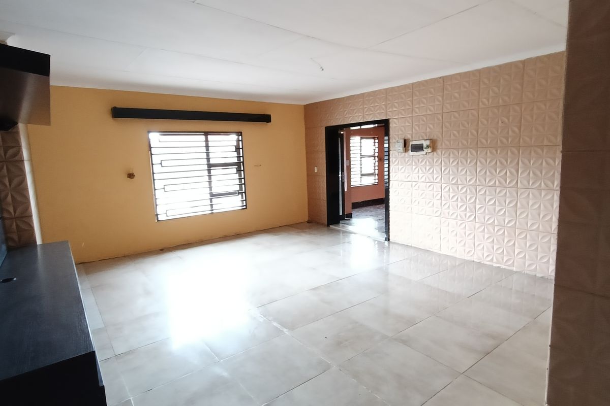 A spacious, empty living area featuring tiled flooring, textured feature walls, and a built-in media unit, offering a blank canvas for personalization.