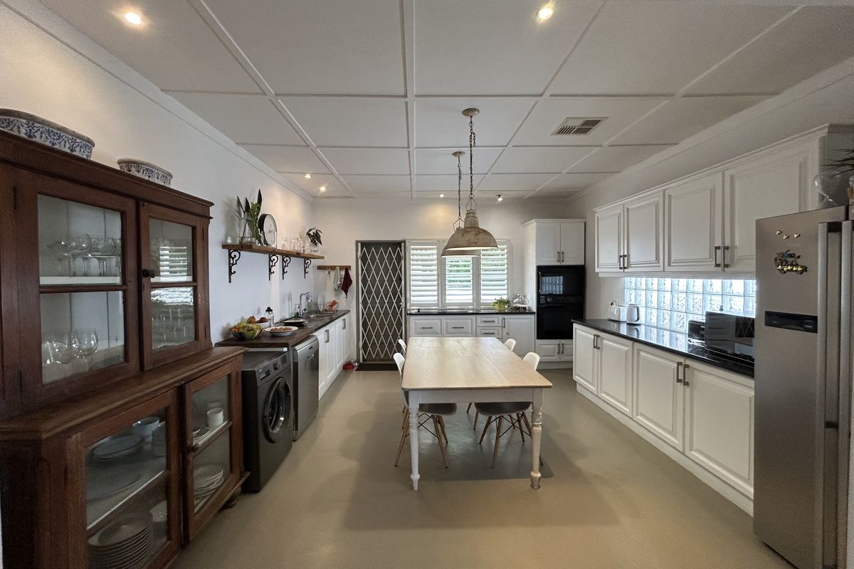 Spacious kitchen featuring white cabinetry, dark countertops, integrated appliances, and a central dining area with a coffered ceiling and glass block accents.