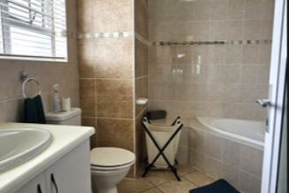A compact bathroom featuring a built-in bathtub, vanity cabinet with basin, and toilet, finished with ceramic floor and wall tiles.