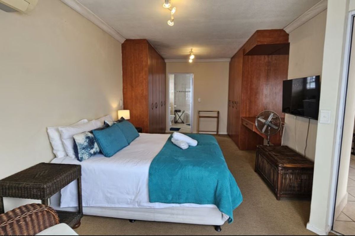 Spacious bedroom featuring extensive built-in wooden cabinetry, carpeted flooring, and an en-suite bathroom access, providing a functional and comfortable living space.