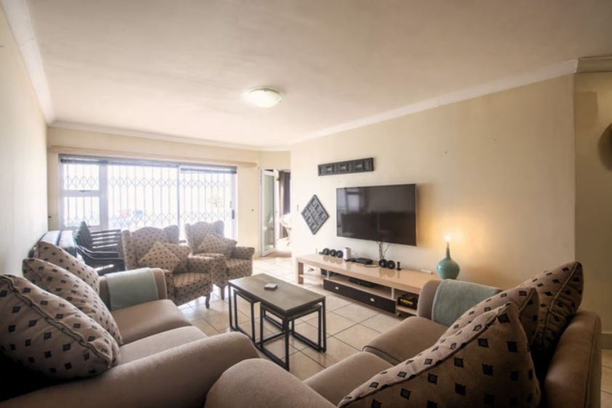 A comfortable living room featuring tiled flooring, large windows with security bars, and a neutral color palette, providing a functional and inviting space.