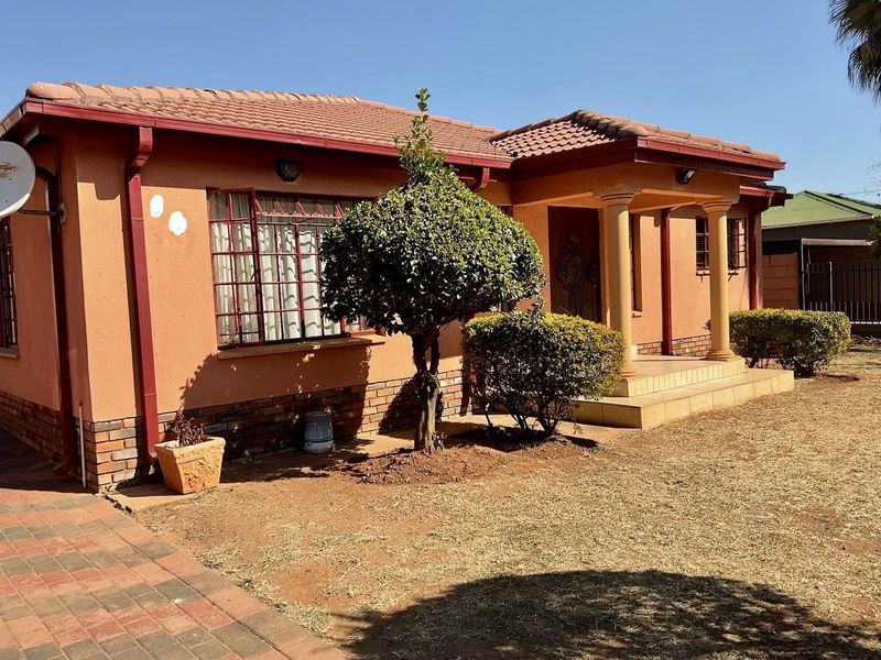 Front elevation of a single-story house featuring a tiled roof, brick accents, security bars on windows, and a covered entrance porch with decorative columns.
