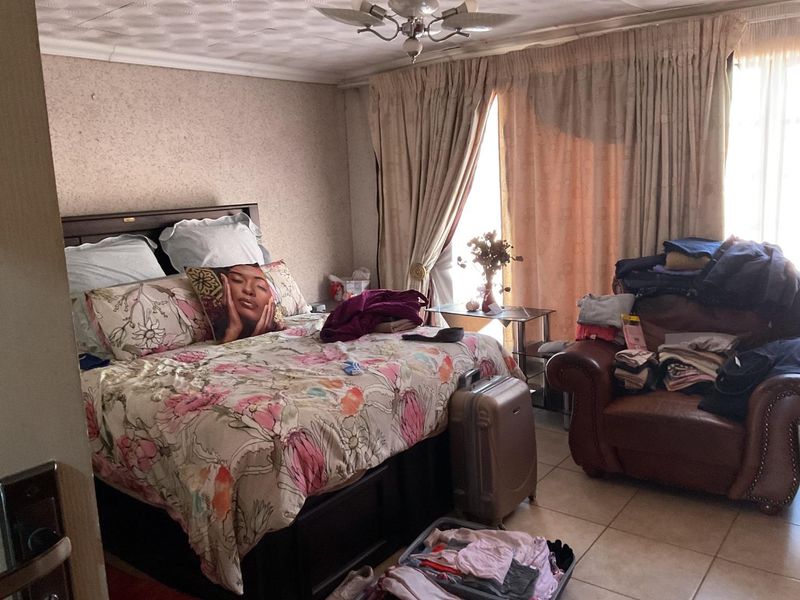 A bedroom featuring tiled flooring and a ceiling fan, with dated wall and ceiling finishes that could benefit from a modern update.