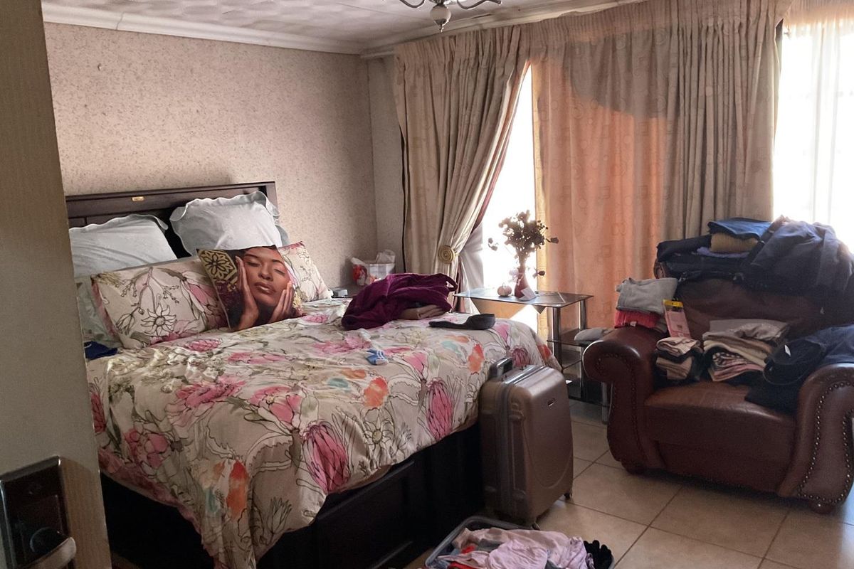 A bedroom featuring tiled flooring and a ceiling fan, with dated wall and ceiling finishes that could benefit from a modern update.