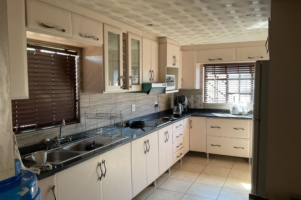 A functional kitchen featuring ample built-in cabinetry, granite countertops, a double basin sink, and tiled flooring with a neutral backsplash.