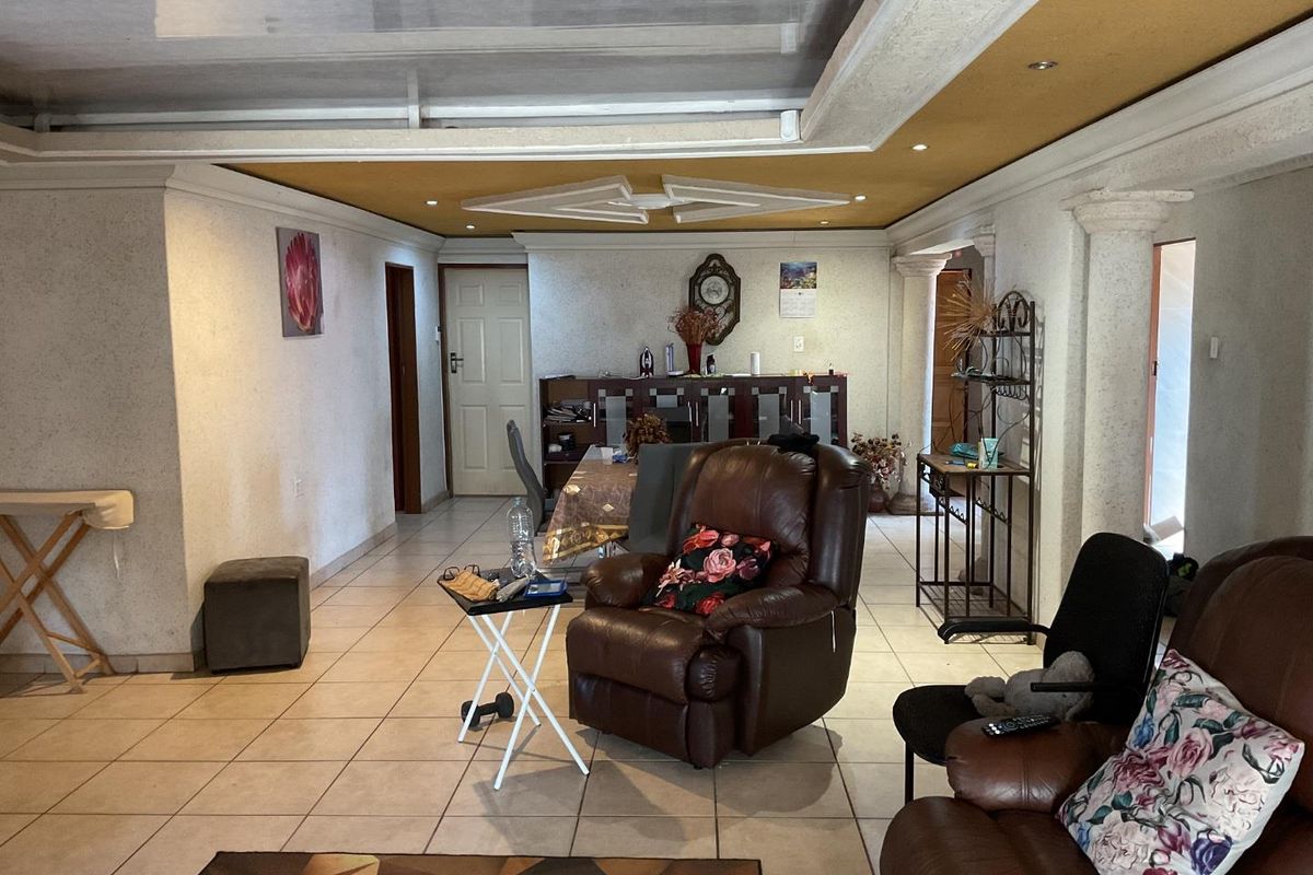 Spacious living area featuring tiled flooring, decorative columns, and a unique ceiling design with recessed lighting, offering potential for modernization.