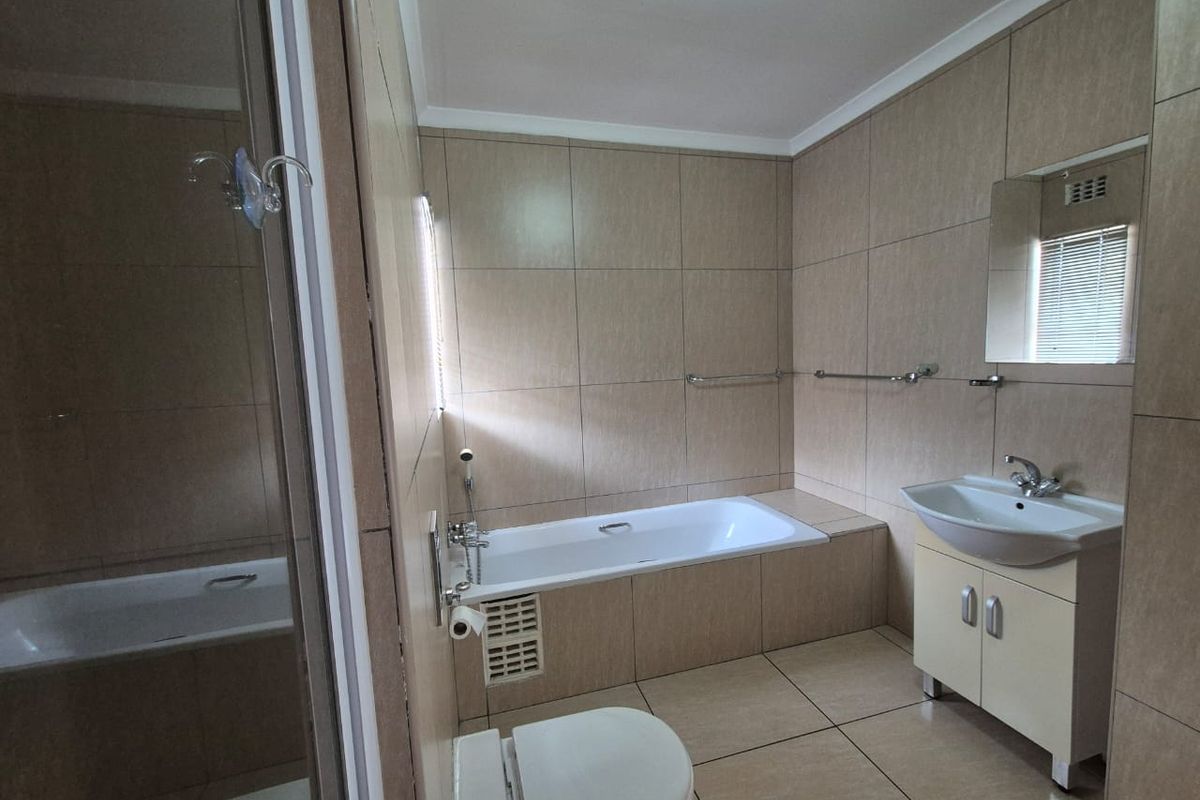 A functional bathroom featuring a built-in bathtub, wall-mounted vanity with basin, and neutral floor-to-ceiling tiling.