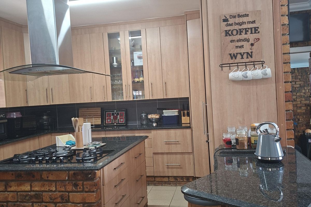 A well-appointed kitchen featuring light wood cabinetry, granite countertops, a central island with a gas hob, and a stainless steel extractor fan.
