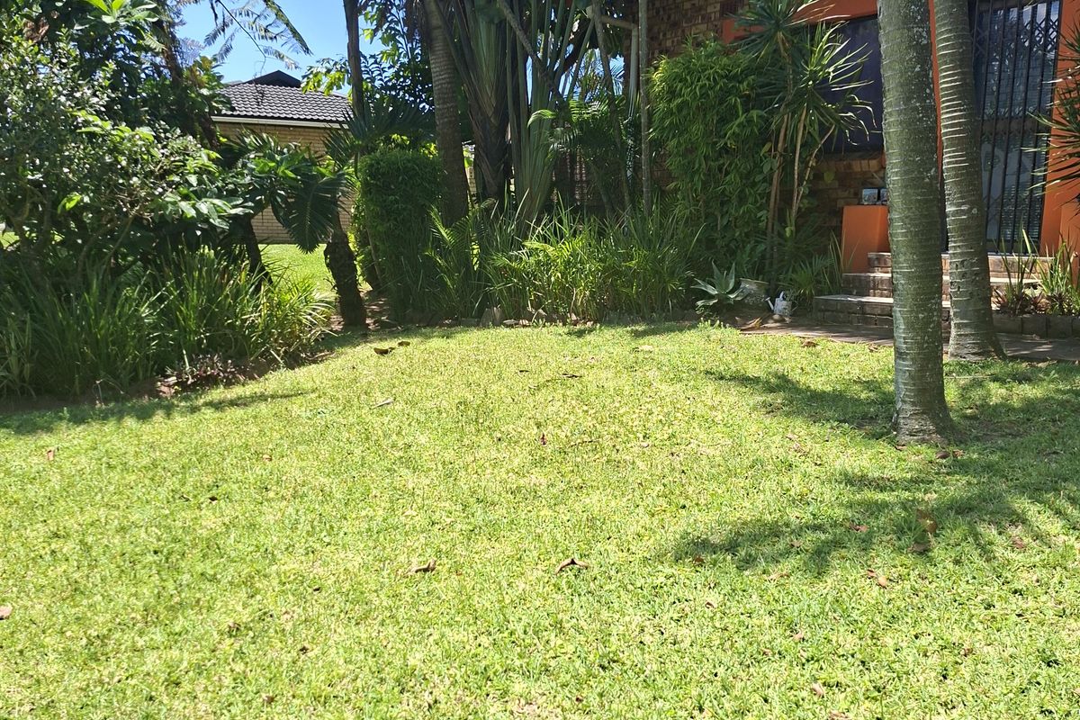 A view of the rear garden featuring a well-maintained lawn, mature trees, and established landscaping adjacent to the house exterior.