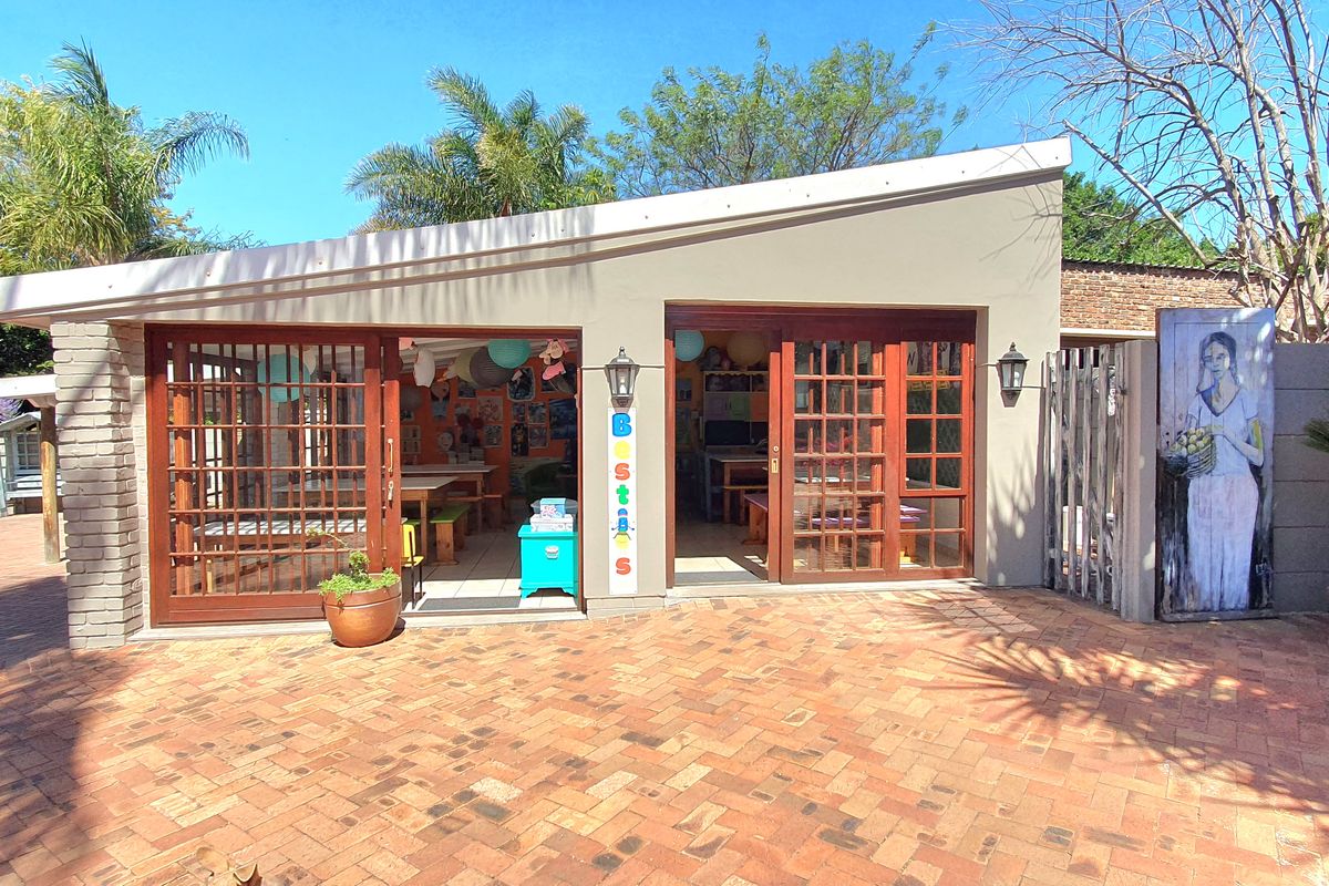 A well-maintained outdoor entertainment area featuring a paved courtyard, covered patio with wooden French doors, and established garden surroundings.