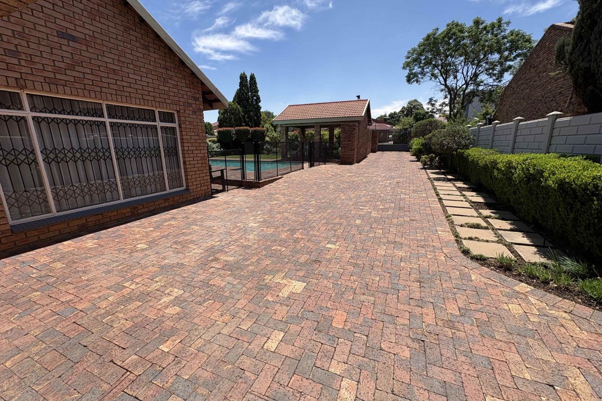 Spacious paved rear courtyard featuring a swimming pool, covered entertainment area, and well-maintained garden borders.