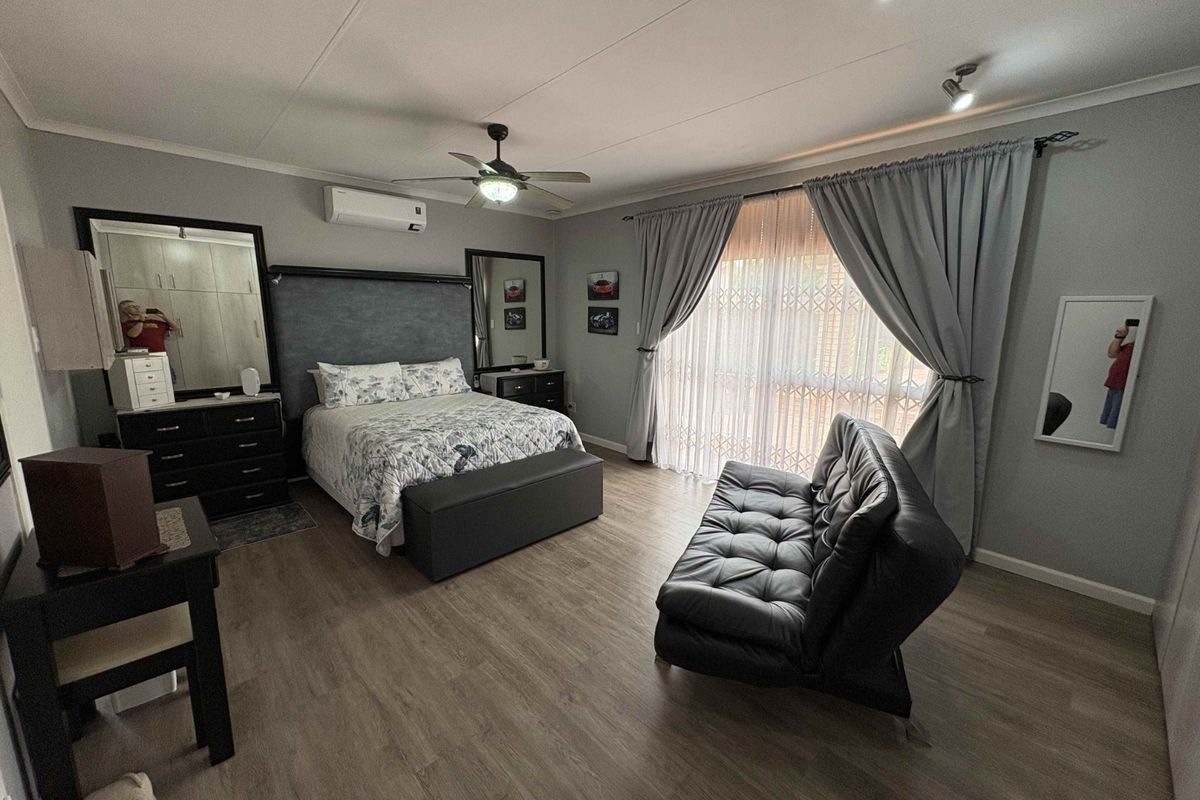 Spacious bedroom featuring wood-look flooring, a ceiling fan, and a wall-mounted air conditioning unit, with large sliding doors leading to an outdoor area.