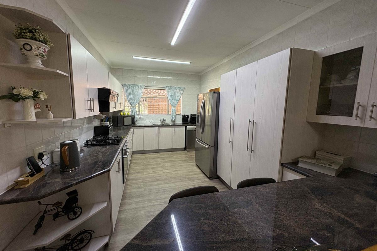 A functional kitchen featuring granite countertops, built-in cabinetry, a gas hob, and tiled flooring with ample storage space.