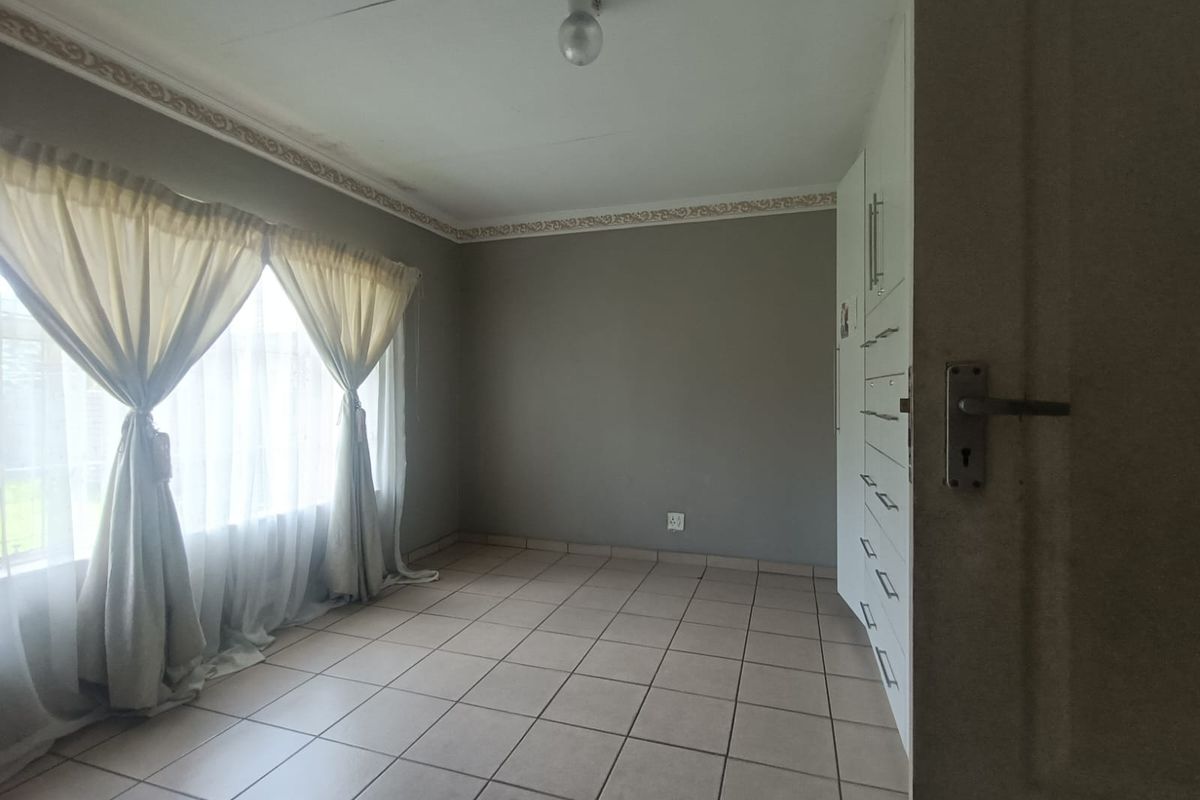 A bright, empty bedroom featuring neutral tiled flooring, built-in cabinetry, and decorative ceiling cornicing.