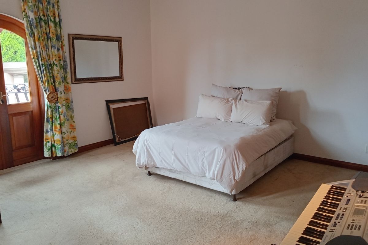 A spacious bedroom featuring neutral carpeting, a wooden arched door with glass panels, and direct access to an outdoor area.