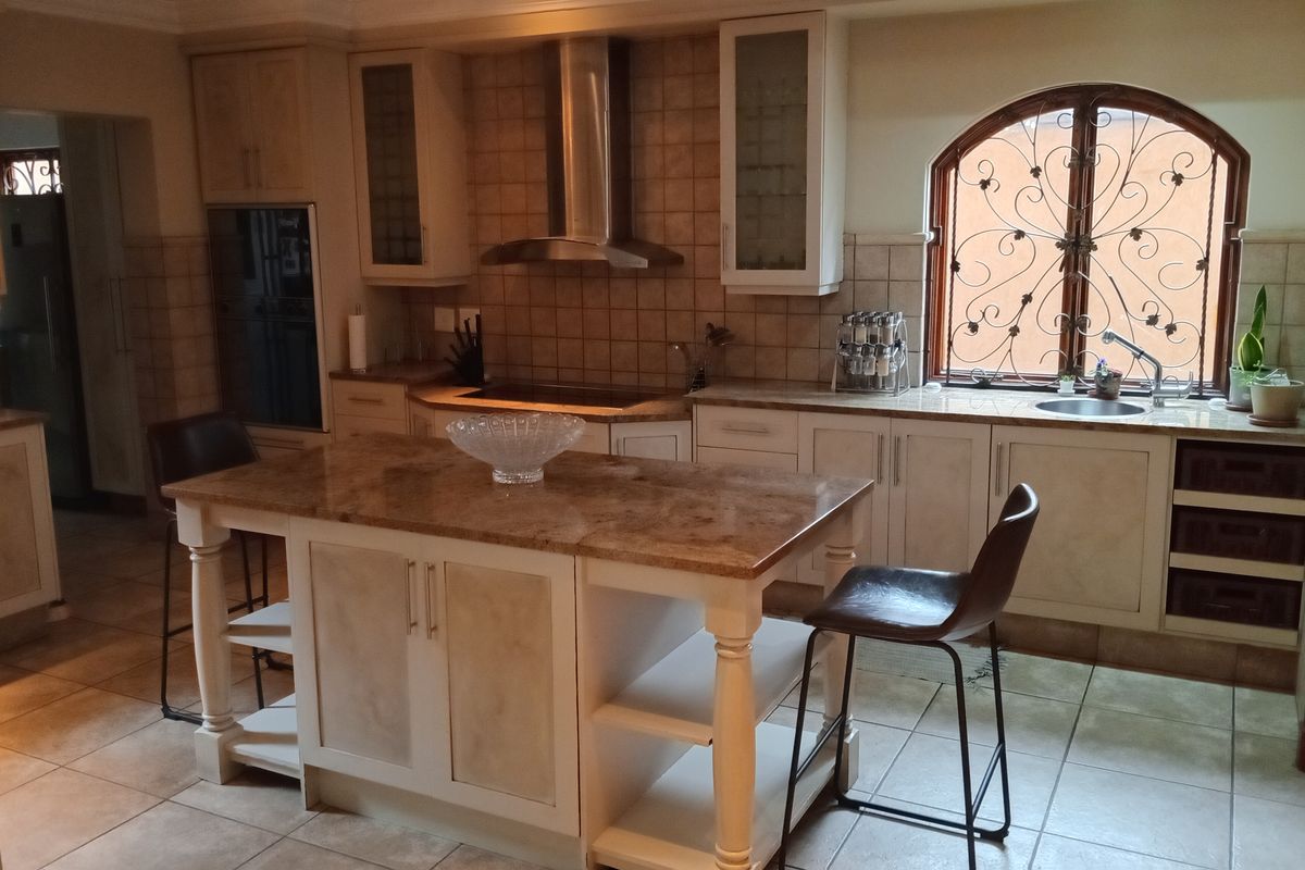 A traditional kitchen featuring a central island with stone countertop, built-in oven, stainless steel extractor fan, and a decorative arched window with security bars.