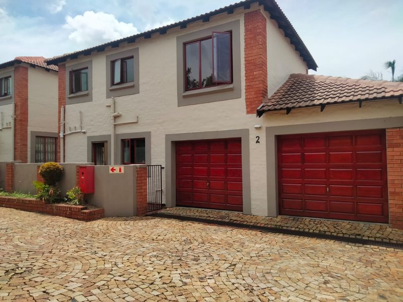 Front elevation of a townhouse featuring a double garage, textured facade with brick accents, and a cobblestone driveway.